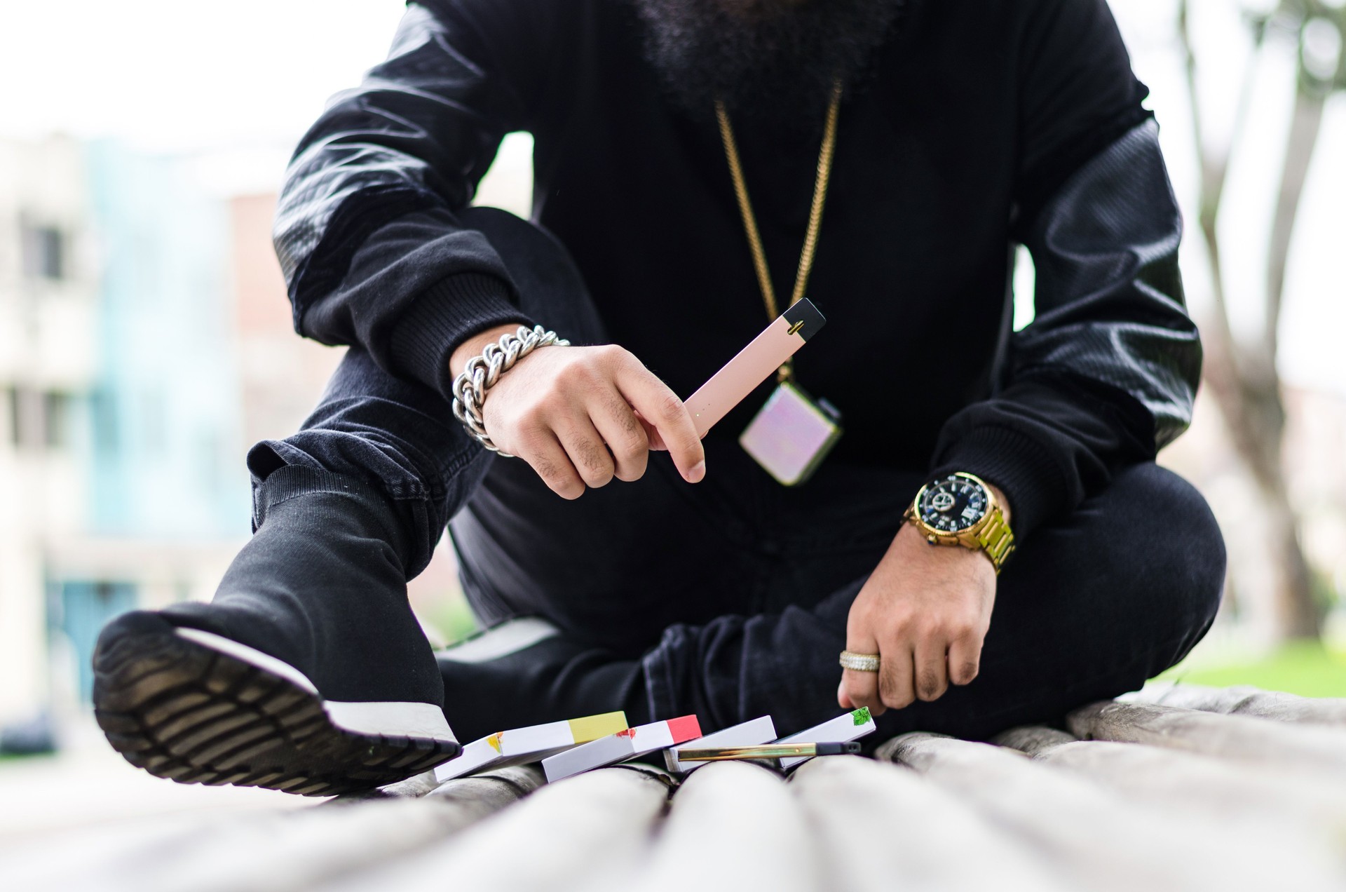 man with a beard smokes an electronic cigarette sit on a bench