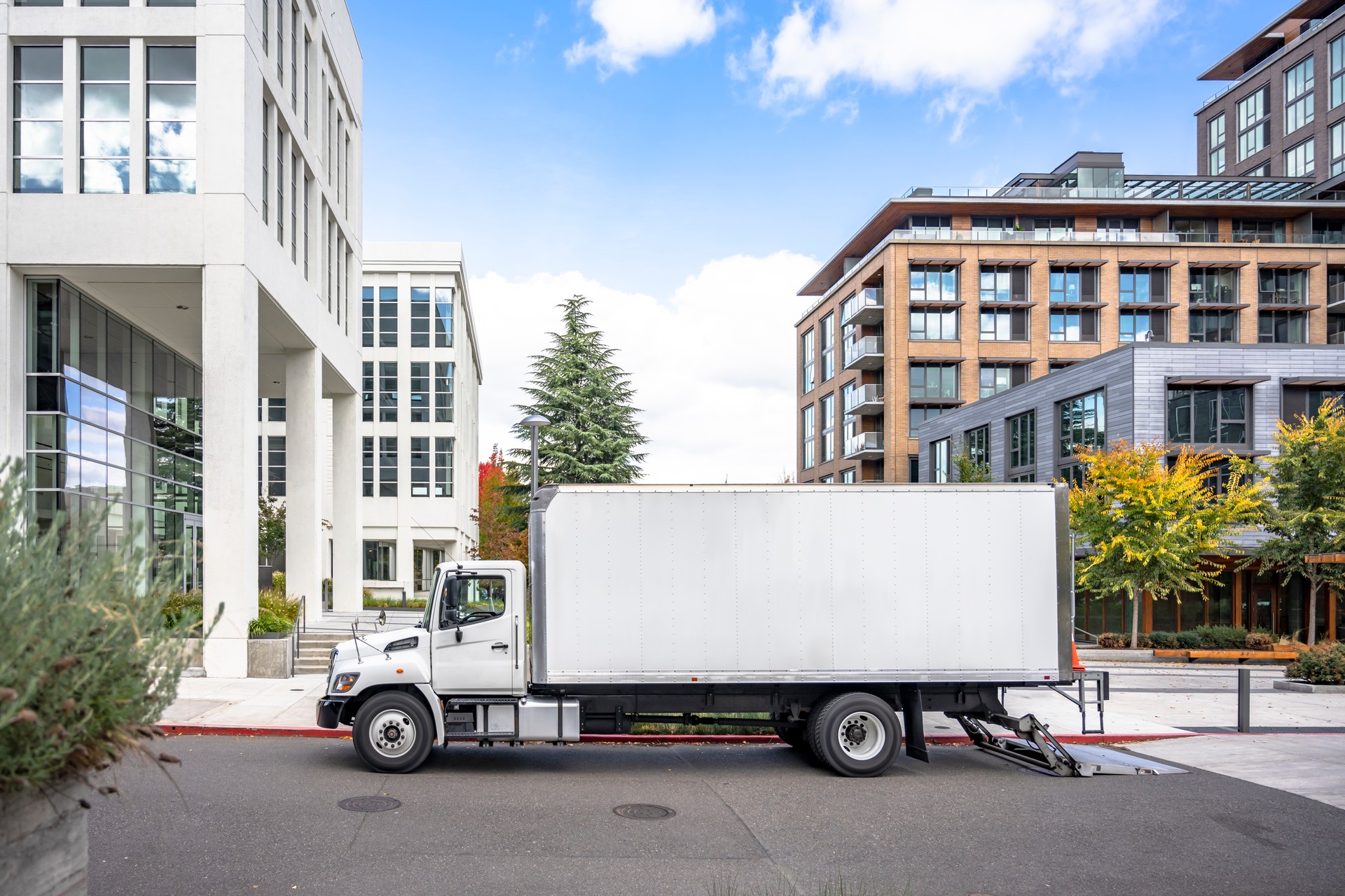 Profile of day cab medium size semi truck with long box trailer unloaded delivered goods to new multi-level apartments in unban city area